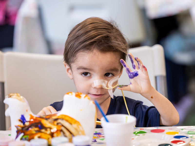 Children's of Mississippi patient Jaxx McDaniel has a colorful wave after a morning painting session with members of the PGA TOUR Wives Association. Jay Ferchaud/ UMMC Photography